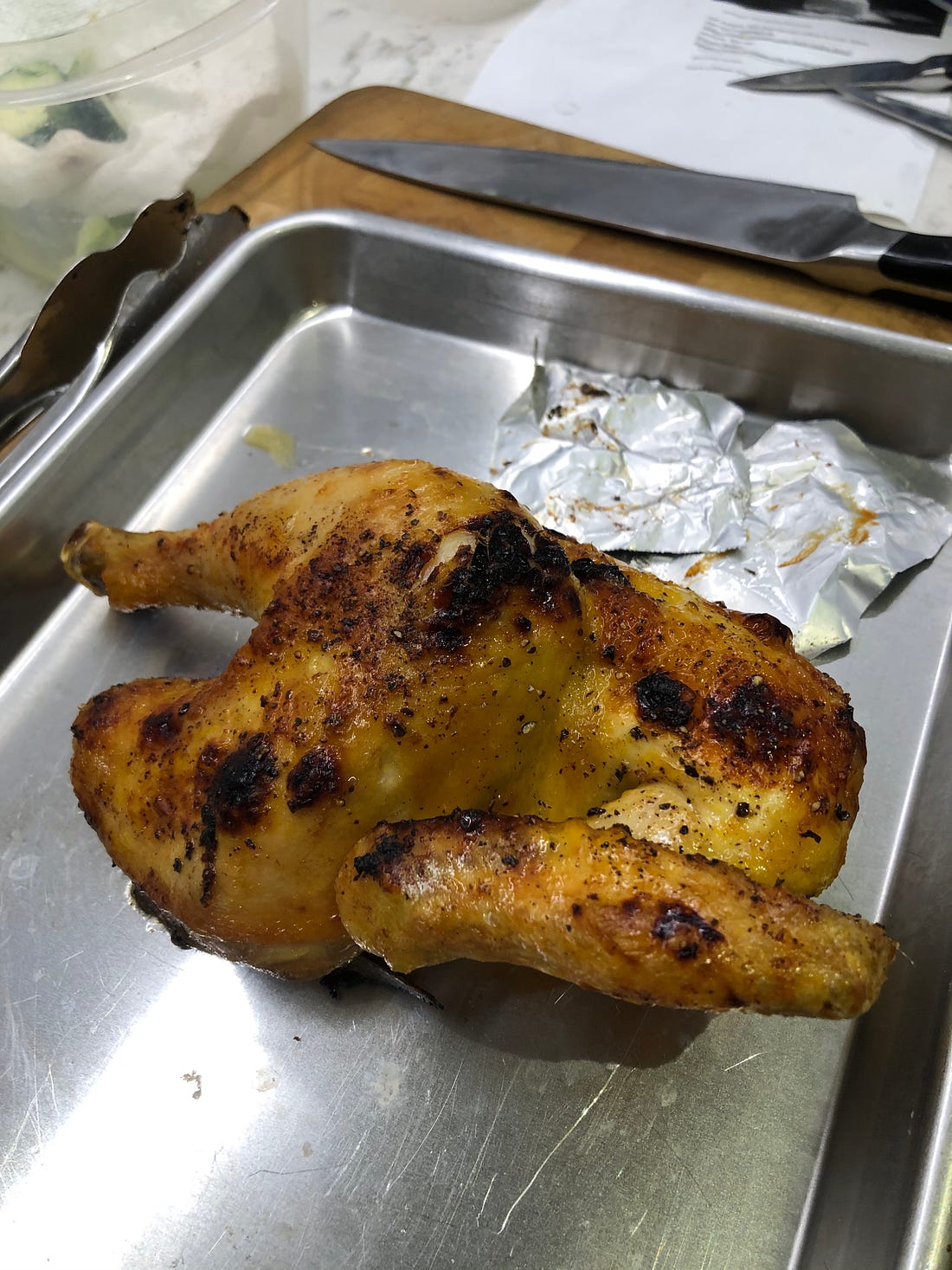 Roasted half chicken on a sheet pan. The skin is burnt in a few places. 