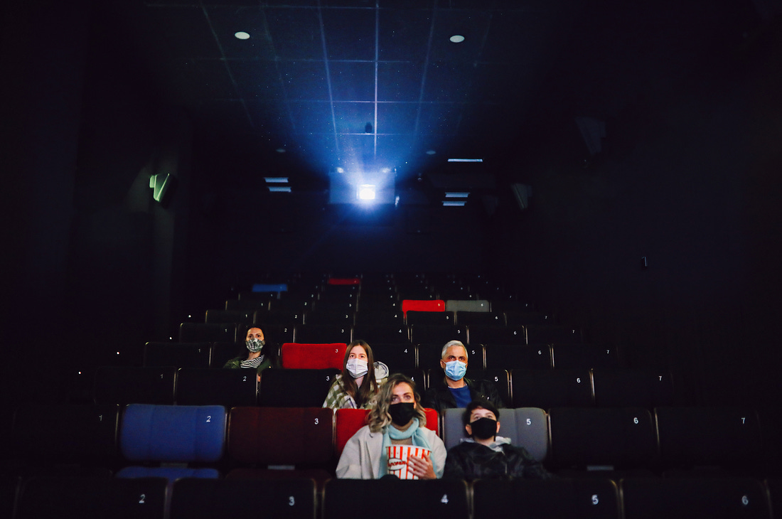 Sala de cinema durante a pandemia, com capacidade reduzida e pessoas usando máscara.
