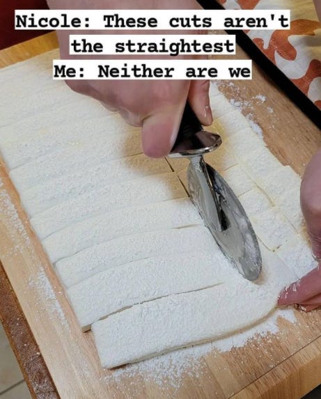 Photo of hands using a pizza cutter to cut a large slab of marshmallow into cubes. It is sitting on a wood cutting board. There is powdered sugar everywhere. There is text that reads, “Nicole: These cuts aren’t the straightest. Me: Neither are we.”