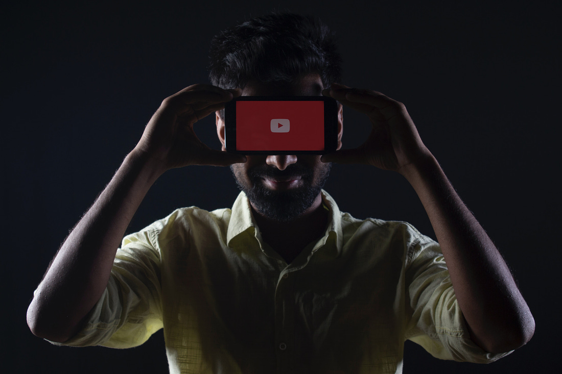 A man holds a phone showing YouTube's logo on his forehead. Photo by Ratchit Tank / Unsplash