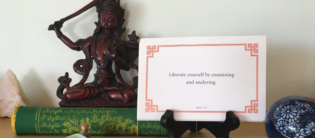 A Lojong card that reads “Liberate yourself by examining and analyzing” sits on a wooden shrine, to the right of a statue of the Bodhisattva Manjushri.
