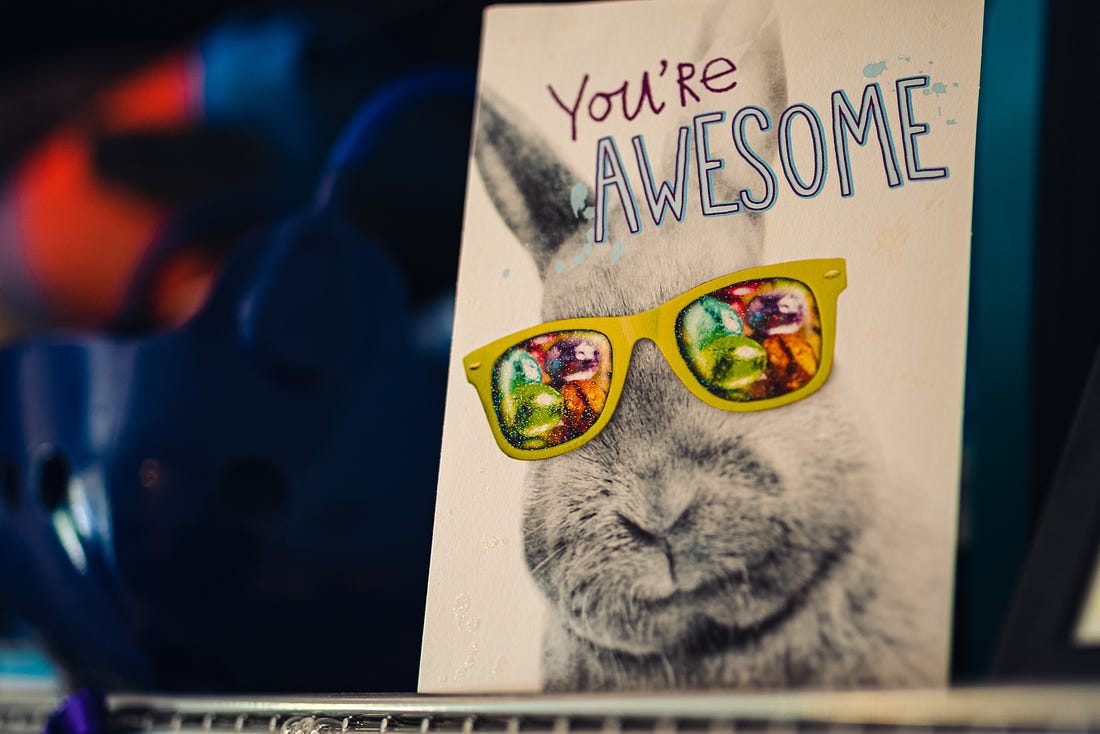 A greeting card propped on a shelf reads "You're AWESOME" above a rabbit with sunglasses. 