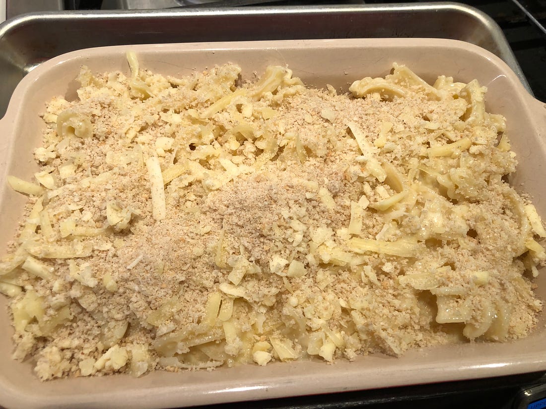 A baking dish filled with pasta and sauce, covered in a mixture of cheese and bread crumbs, ready for the oven