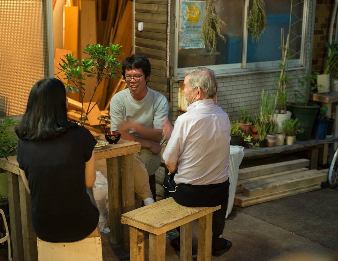 Neighbors enjoy food and drink outside a home in an alleyway in Osaka, Japan