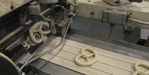 Automation: a machine folds dough into a pretzel shape on a conveyor belt [gif]