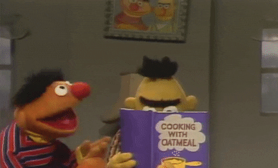 Bert reading a book called "Cooking with Oatmeal" and Ernie talking to him