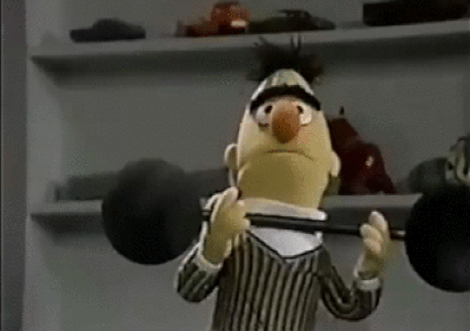 Bert trying to carry and dropping a large dumbbell. ernie giggles.