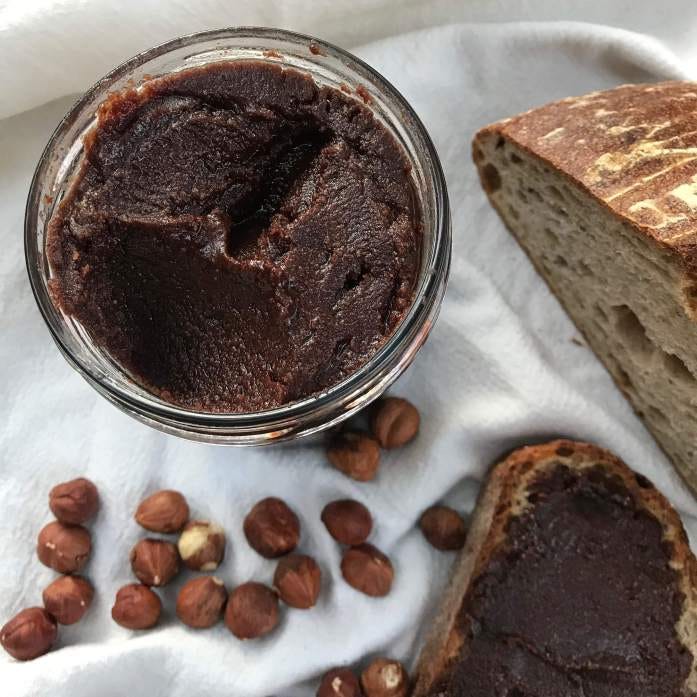 a jar of hazelnut chocolate spread with some sourdough bread in the background and a handful of hazelnuts a jar of hazelnut chocolate spread with some sourdough bread in the background and a handful of hazelnuts