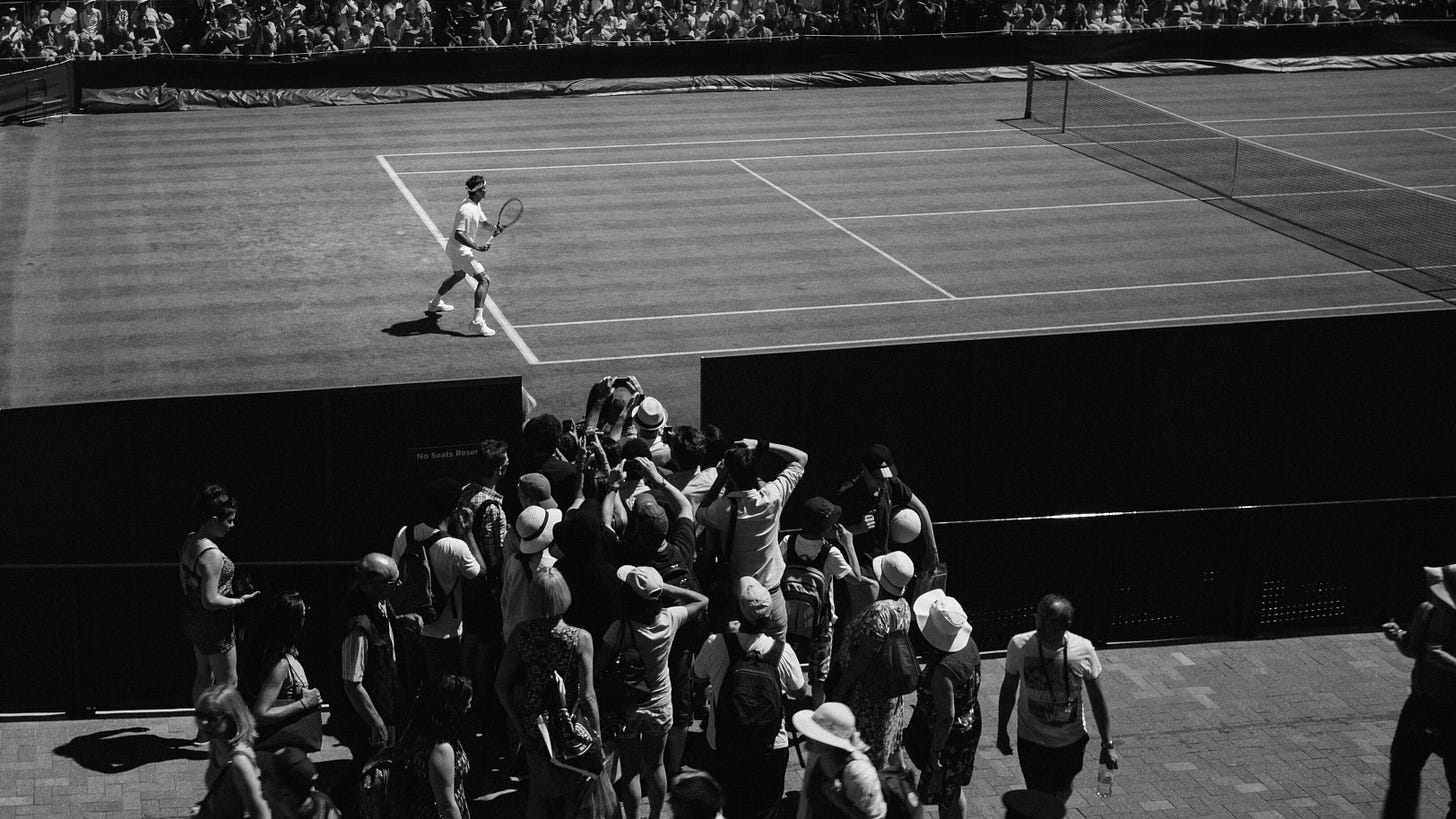 A group of spectators crowd on the sidelines to take photos of a tennis player. A group of spectators crowd on the sidelines to take photos of a tennis player.