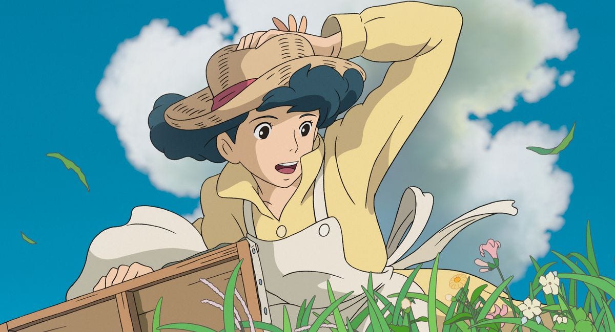 A woman in a green, flowery field clutches her hat against the wind in The Wind Rises