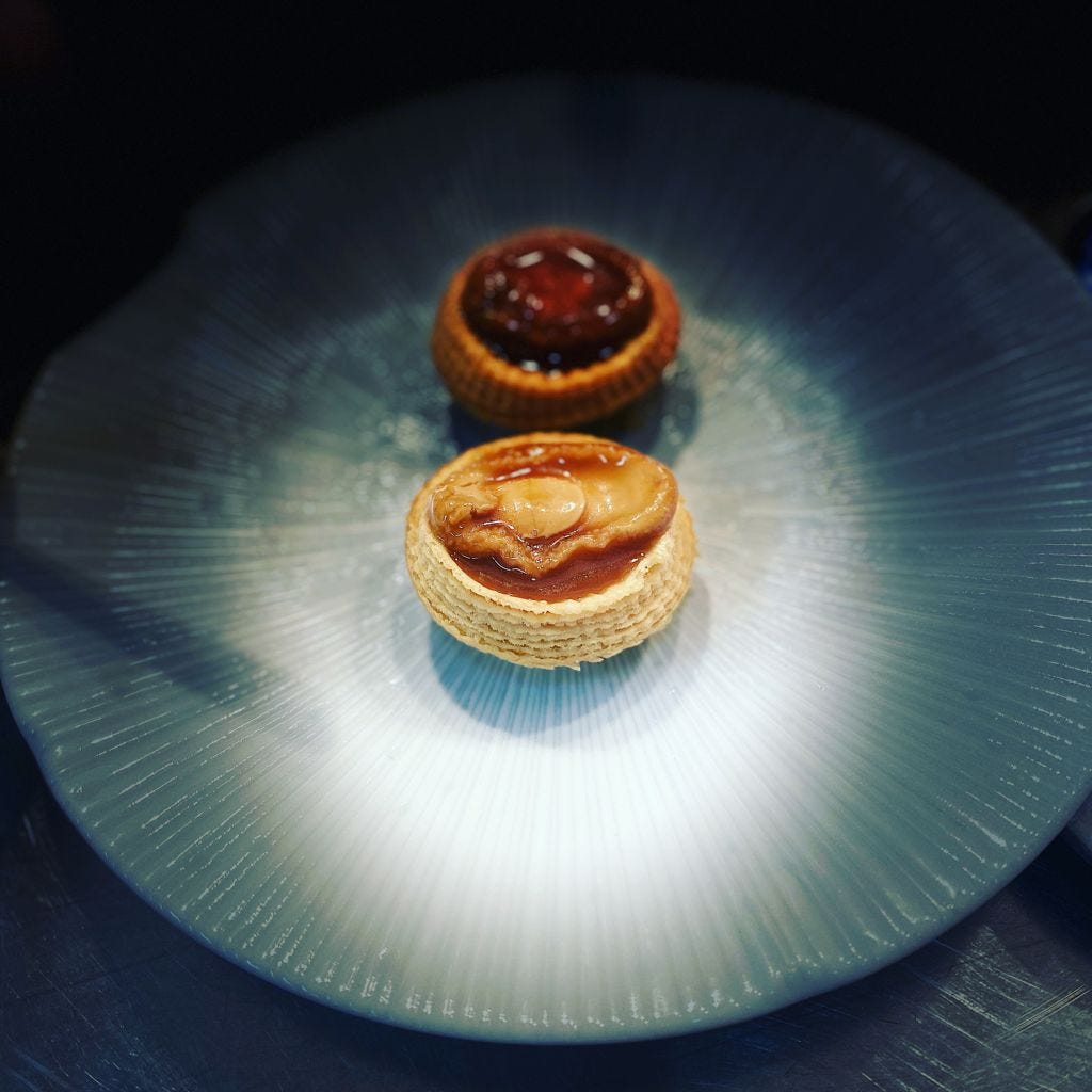 A sideview of a cooked abalone encase in a pastry tart case in the centre of a textured dinner plate A sideview of a cooked abalone encase in a pastry tart case in the centre of a textured dinner plate