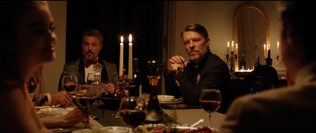 From the film 'The Dinner Party': Two men stare inquisitively and ominously, across a fine dining table, from a woman on the left of the screen, looking at her husband on the right. From the film 'The Dinner Party': Two men stare inquisitively and ominously, across a fine dining table, from a woman on the left of the screen, looking at her husband on the right.