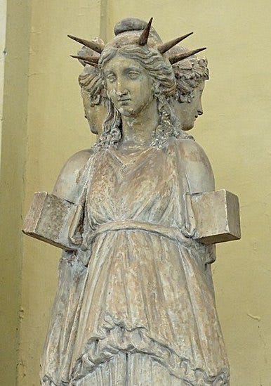 We see the upper part of an unpainted Roman stone copy of a Greek statue: three women standing back-to-back, their arms ending strangely in cubes right below the shoulder; the one facing the camera wears a spiked crown with no spike right over her brow. We see the upper part of an unpainted Roman stone copy of a Greek statue: three women standing back-to-back, their arms ending strangely in cubes right below the shoulder; the one facing the camera wears a spiked crown with no spike right over her brow.