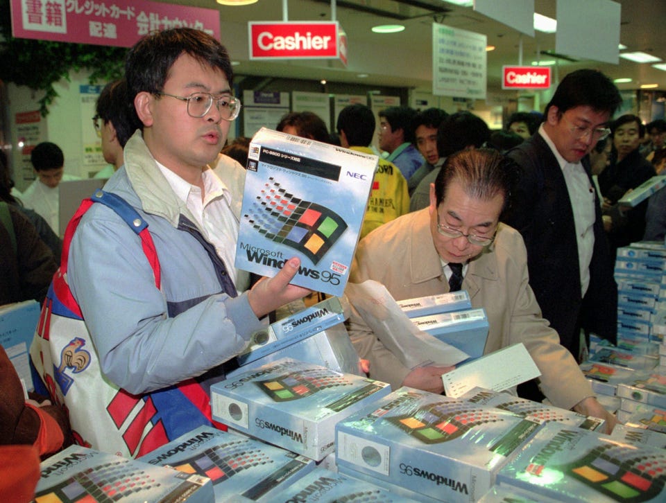Foto mostra uma pessoa segurando uma caixa com CDs ou disquetes de instalação do Windows 95, enquanto outras pessoas olham mais caixas do mesmo tipo em um stand de loja. Foto mostra uma pessoa segurando uma caixa com CDs ou disquetes de instalação do Windows 95, enquanto outras pessoas olham mais caixas do mesmo tipo em um stand de loja.