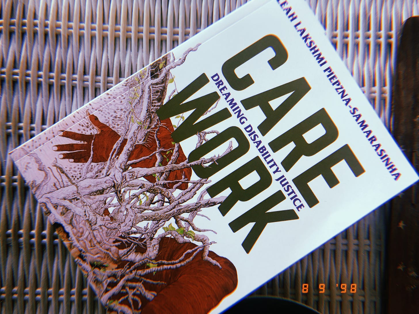 care work, a book with a white cover and dark green title text and an image of a orangeish brown arm and leg emerging from behind a tangle of white roots, sits on top of a wicker dresser