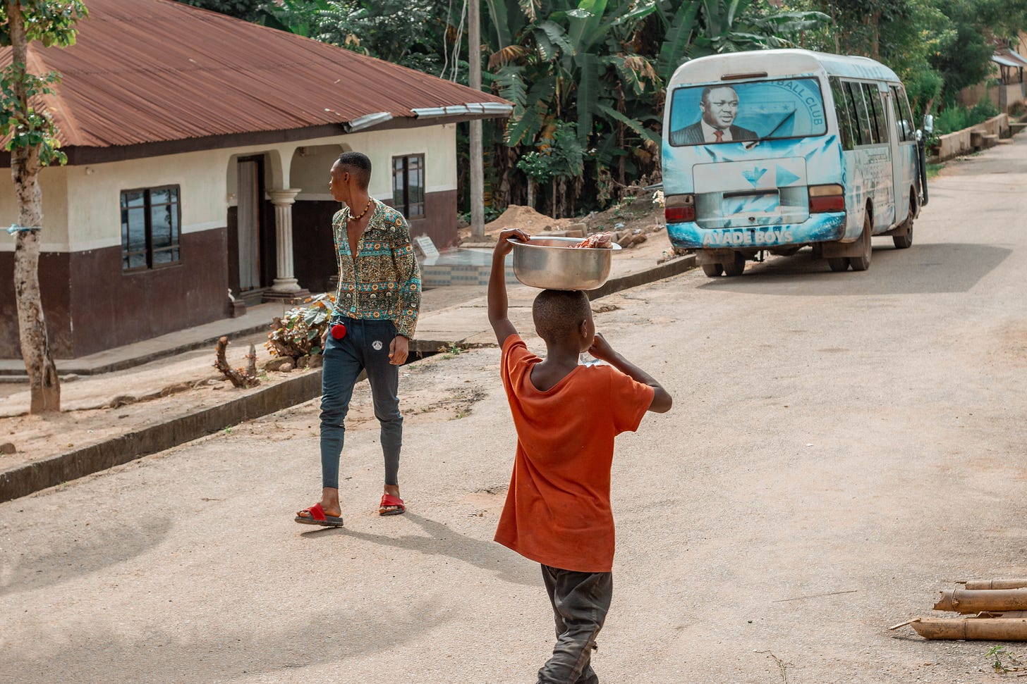  A boy carrying tin container walking the opposite direction to an adult man in Ediba: A photo by David Elikwu