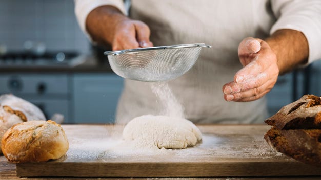 Premium Photo | Close-up of baker sifting the wheat flour through sieve  over dough
