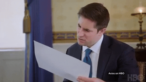 A reporter scrunches up his face, looking at a chart for a data point that has been misread by an off-screen companion [gif]