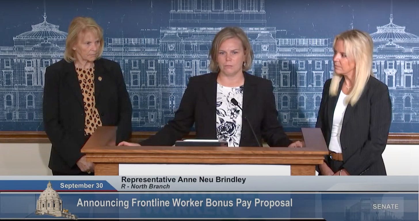 Three blonde white women wearing black blazers stand behind the podium with stern faces