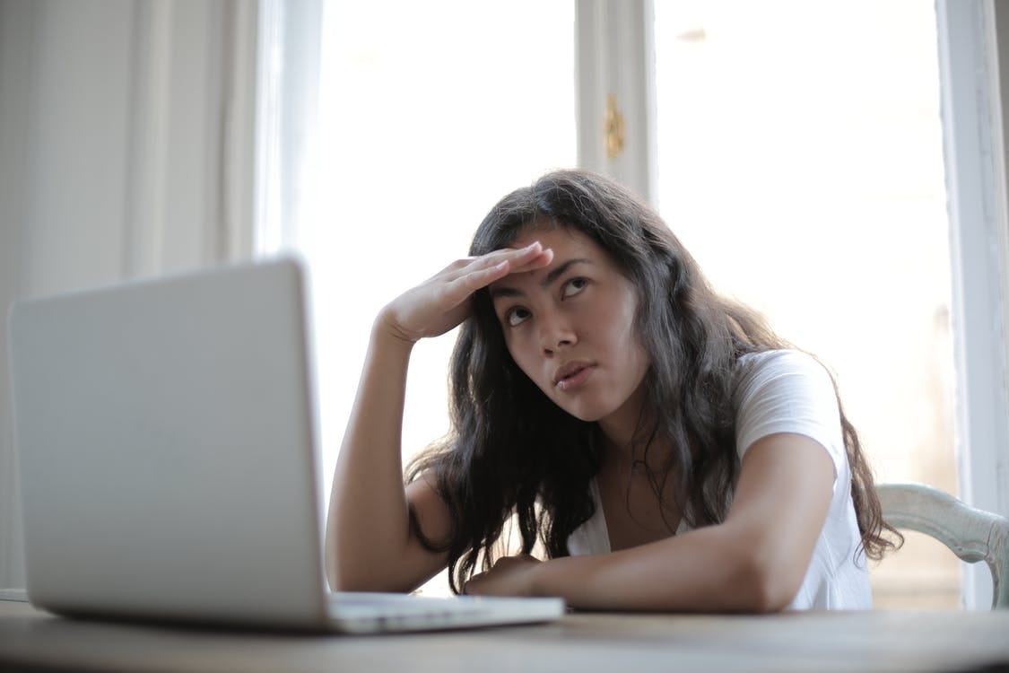 Irritated ethnic female entrepreneur in casual wear sitting at table with netbook and touching head while waiting for internet connection during remote work Irritated ethnic female entrepreneur in casual wear sitting at table with netbook and touching head while waiting for internet connection during remote work