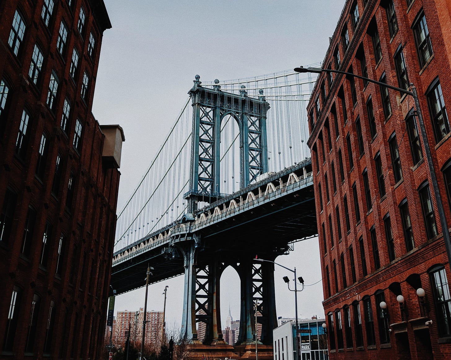 Photo of the Brooklyn Bridge between two brick buildings. Photo of the Brooklyn Bridge between two brick buildings.
