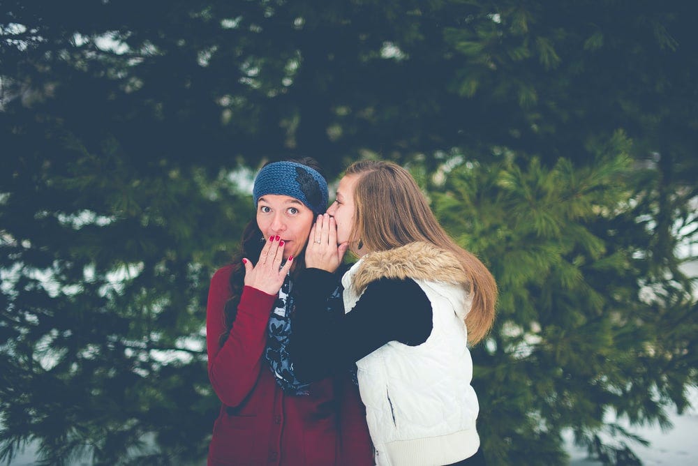 woman whispering on woman's ear while hands on lips woman whispering on woman's ear while hands on lips
