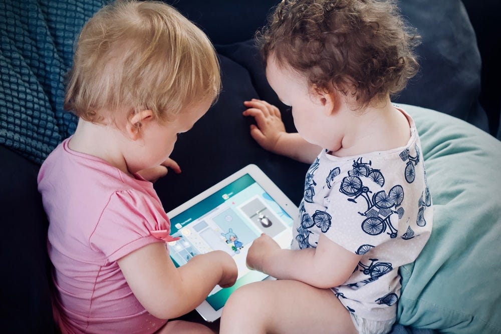 two toddlers sitting on sofa while using tablet computer two toddlers sitting on sofa while using tablet computer