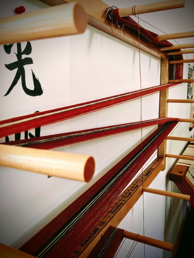 Photograph of orange, white, and navy coloured thread being wound on a pegged warping board to create a warp chain. Photograph of orange, white, and navy coloured thread being wound on a pegged warping board to create a warp chain.