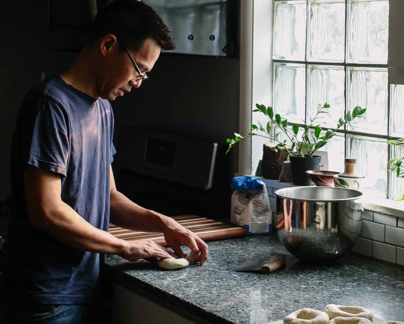 Jeff stands at a granite kitchen counter rolling dough into bagels