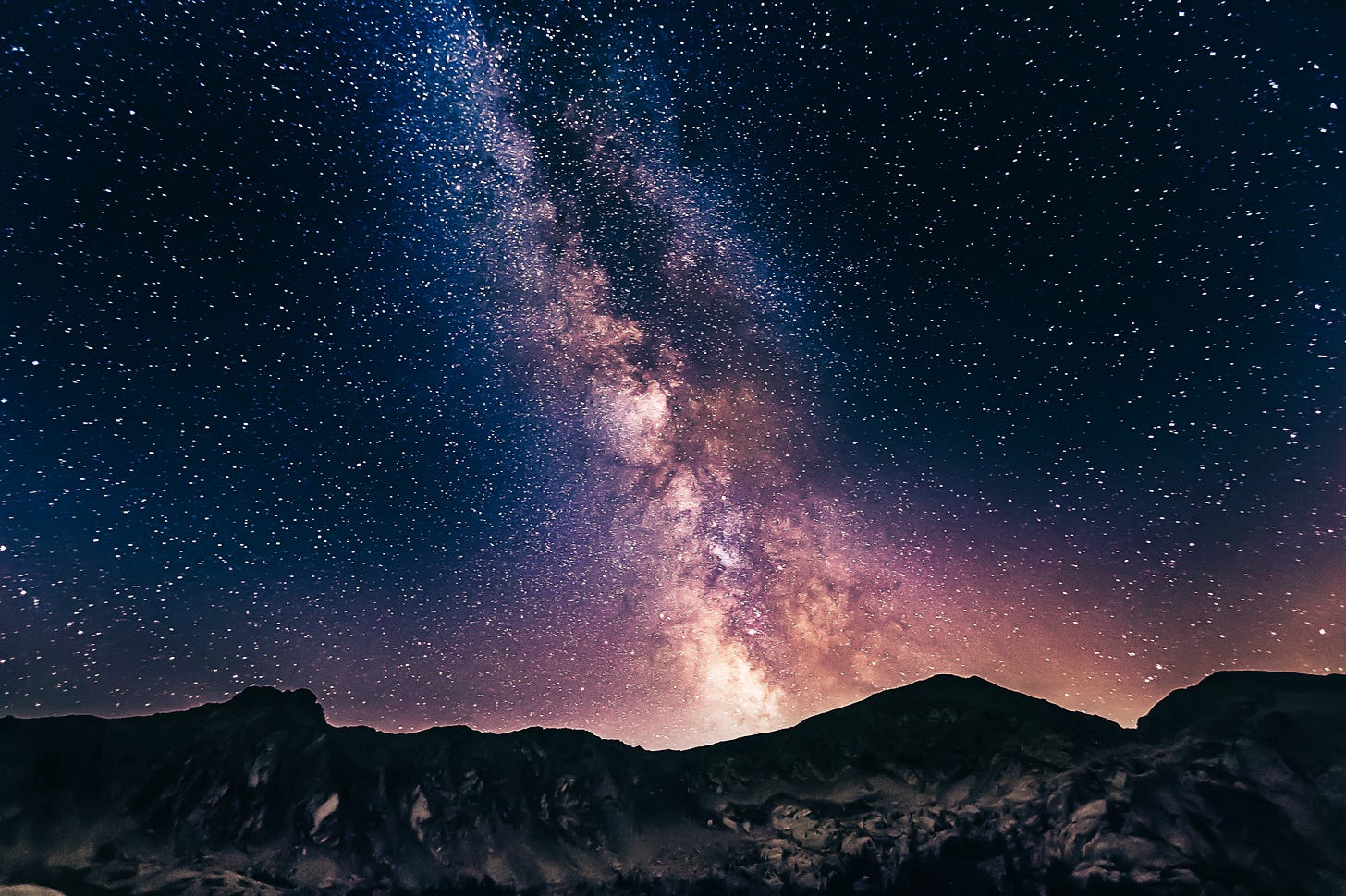 A night sky broken up by a colorful pattern in the middle. A line of bright orange and red clusters of stars is in the middle, while the rest of the stars are normal and blue. A night sky broken up by a colorful pattern in the middle. A line of bright orange and red clusters of stars is in the middle, while the rest of the stars are normal and blue.
