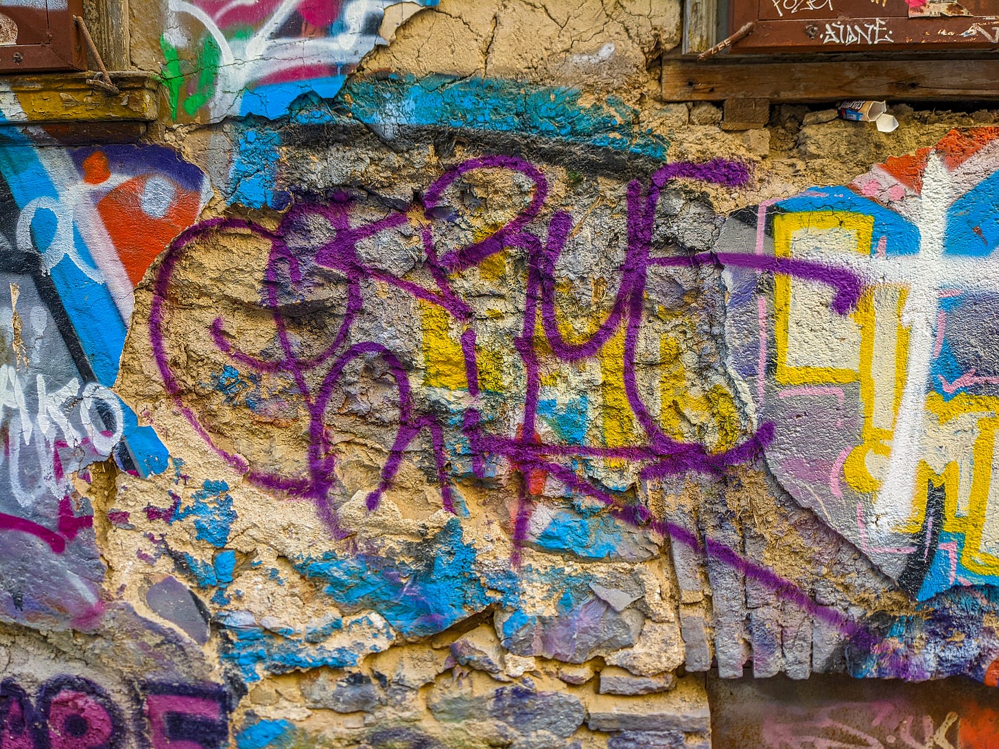 Close-up picture of a wall covered with very colorful graffiti from an unreadable word in purple to big blocky letters and other splashes of color. 