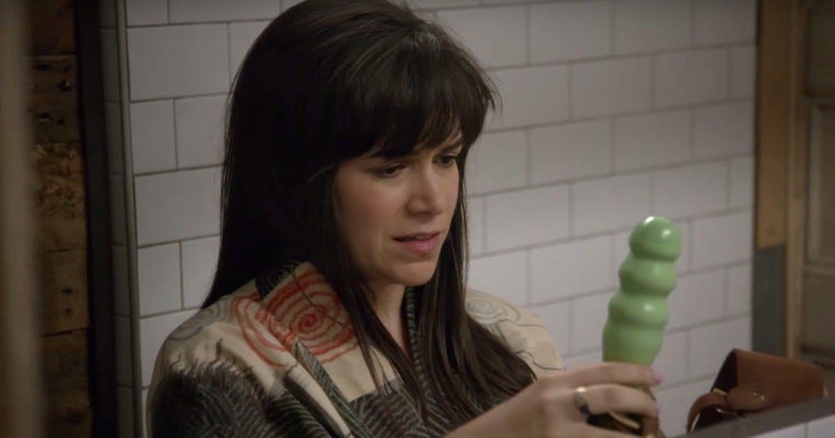 image description: abbi from broad city holding a ribbed strap-on 