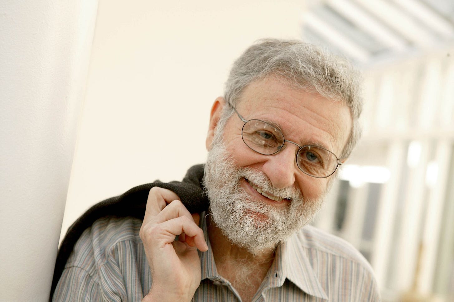 Foto mostra Don Norman, criador das expressões “Design centrado no usuário” e “Experiência do Usuário” em pose informal, de óculos, barba, sorrindo, recostado em uma parede e segurando um casaco no ombro. Foto mostra Don Norman, criador das expressões “Design centrado no usuário” e “Experiência do Usuário” em pose informal, de óculos, barba, sorrindo, recostado em uma parede e segurando um casaco no ombro.
