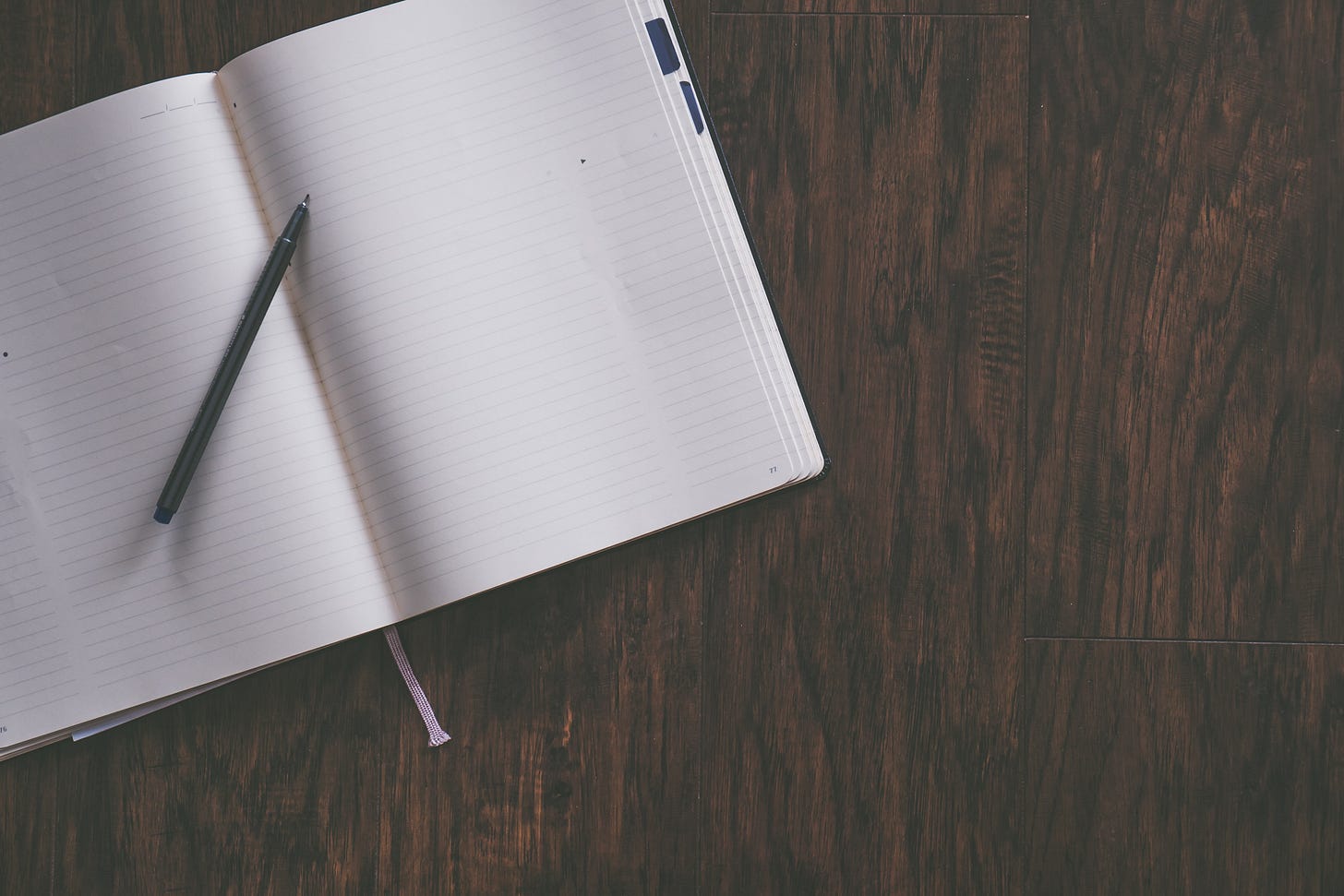 Notebook and pen on a brown wooden desk Notebook and pen on a brown wooden desk