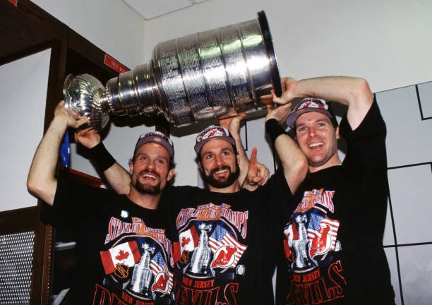 Ken Daneyko, Bruce Driver and John MacLean of the New Jersey Devils hoist the Stanley Cup Trophy over their heads in the locker room after the Devils...