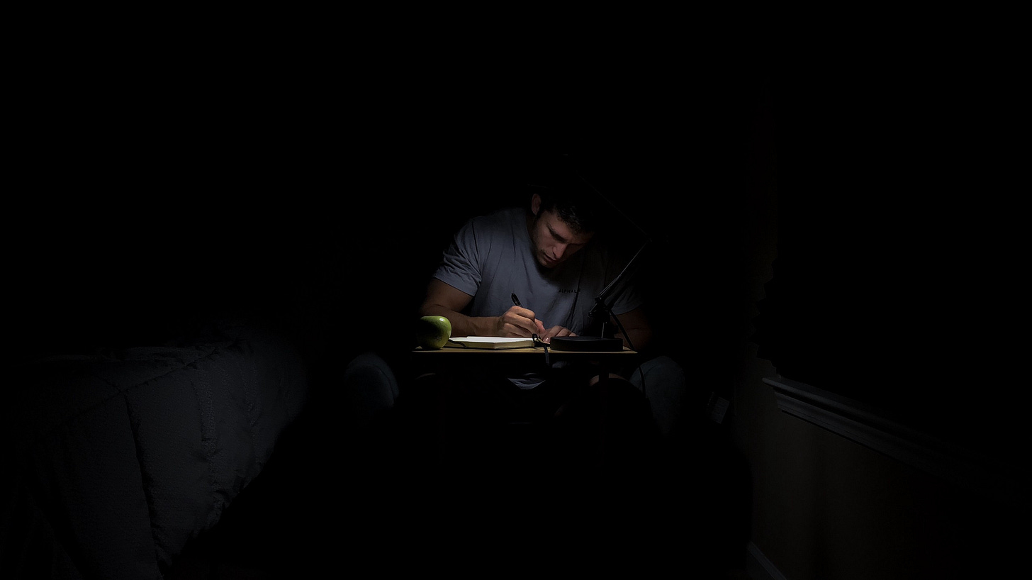 Man sitting in the dark, writing, for article titled “The Book That Never Gets Written” on The Reflectionist Man sitting in the dark, writing, for article titled “The Book That Never Gets Written” on The Reflectionist