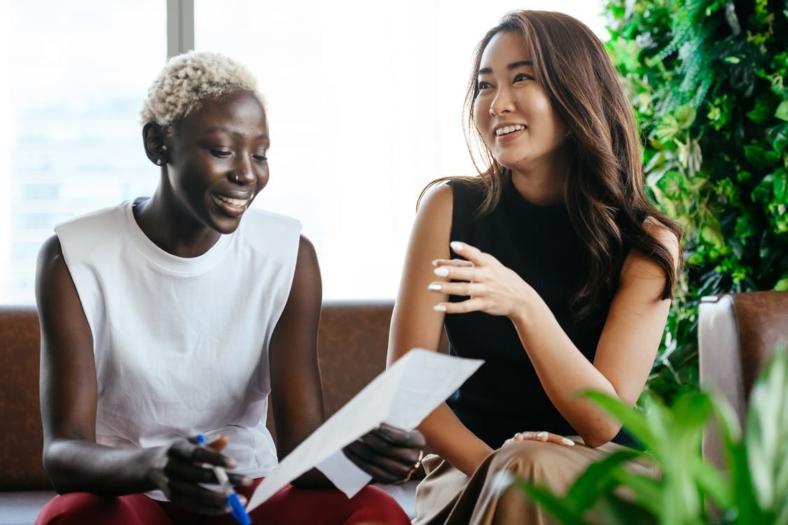 Multiethnic happy smiling women checking papers while speaking in comfortable conference hall in daytime Multiethnic happy smiling women checking papers while speaking in comfortable conference hall in daytime