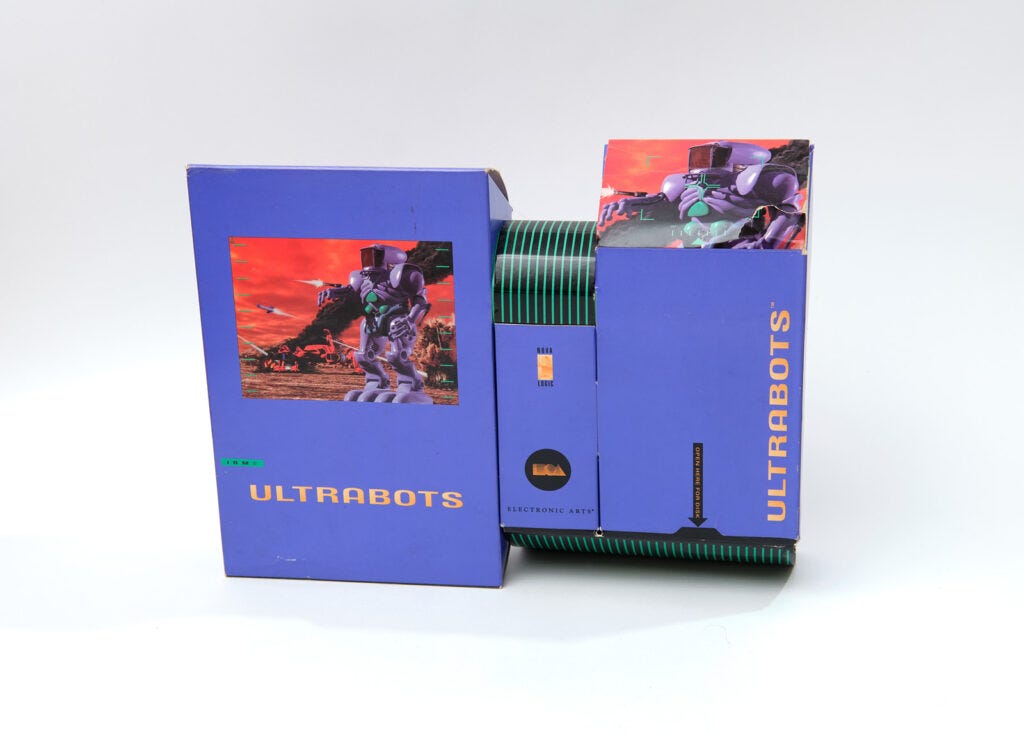 The box for Ultrabots. It consists of three differently-sized rectangular purple boxes stacked next to each other. The boxes are decorated with a combination of game art, featuring a large purple robot, and black-and-green cybernetic stripe patterns. The box for Ultrabots. It consists of three differently-sized rectangular purple boxes stacked next to each other. The boxes are decorated with a combination of game art, featuring a large purple robot, and black-and-green cybernetic stripe patterns.