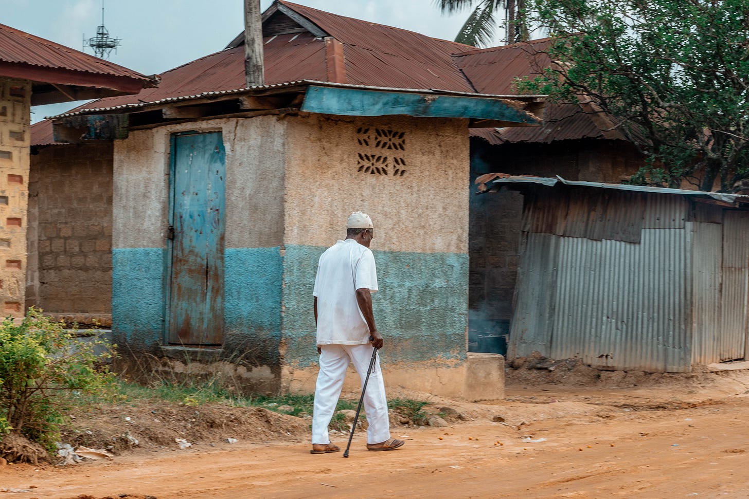 An old man in white pants, shirt and kufi walking in stick in Asaba: A photo by David Elikwu