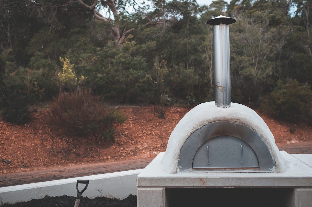 An outdoor oven in front of a backdrop of red earth and green plants.