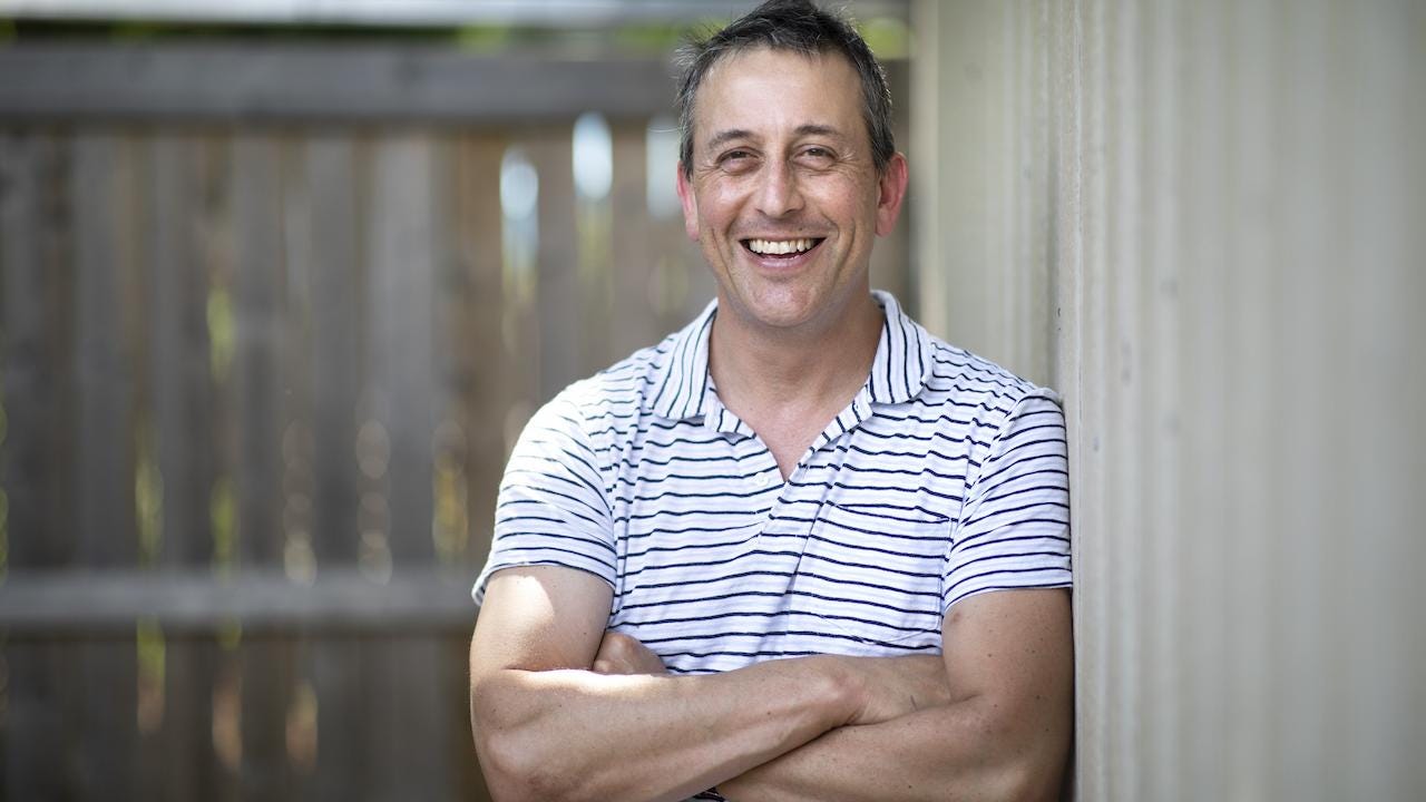 a smiling man with arms crossed wearing a T-shirt