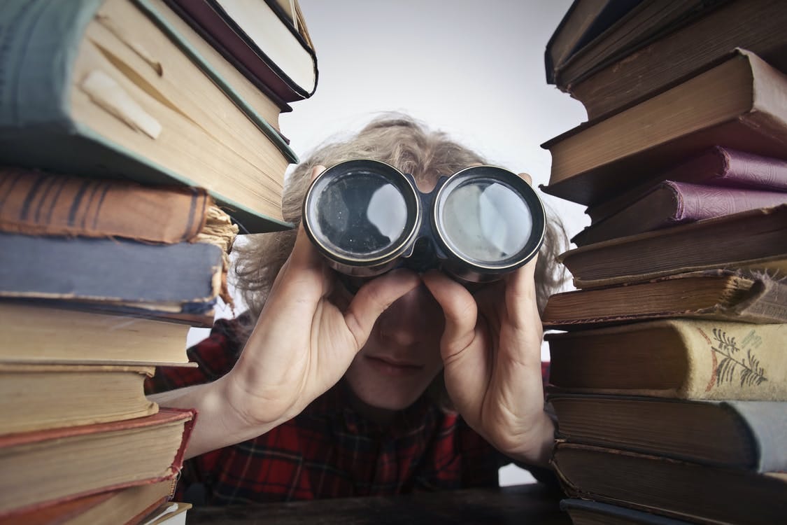 Anonymous person with binoculars looking through stacked books Anonymous person with binoculars looking through stacked books
