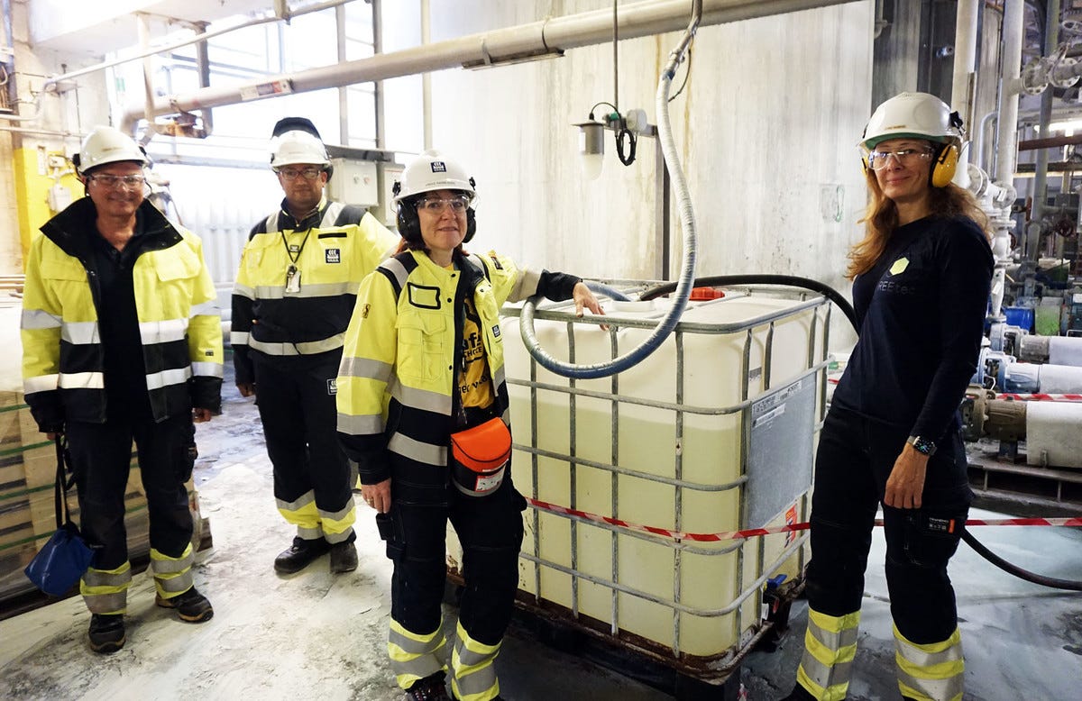 four persons standing around plastic tank with raw material four persons standing around plastic tank with raw material