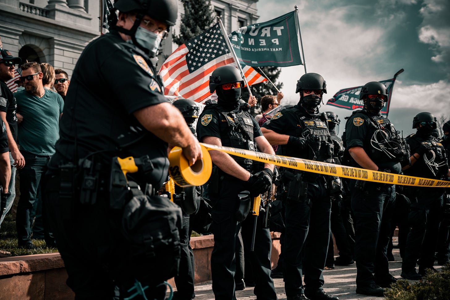 A line of police in riot gear standing in front of "Stop the steal" protesters.