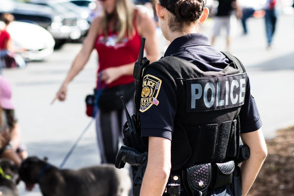 police woman standing near black dog in front of woman wearing red top police woman standing near black dog in front of woman wearing red top