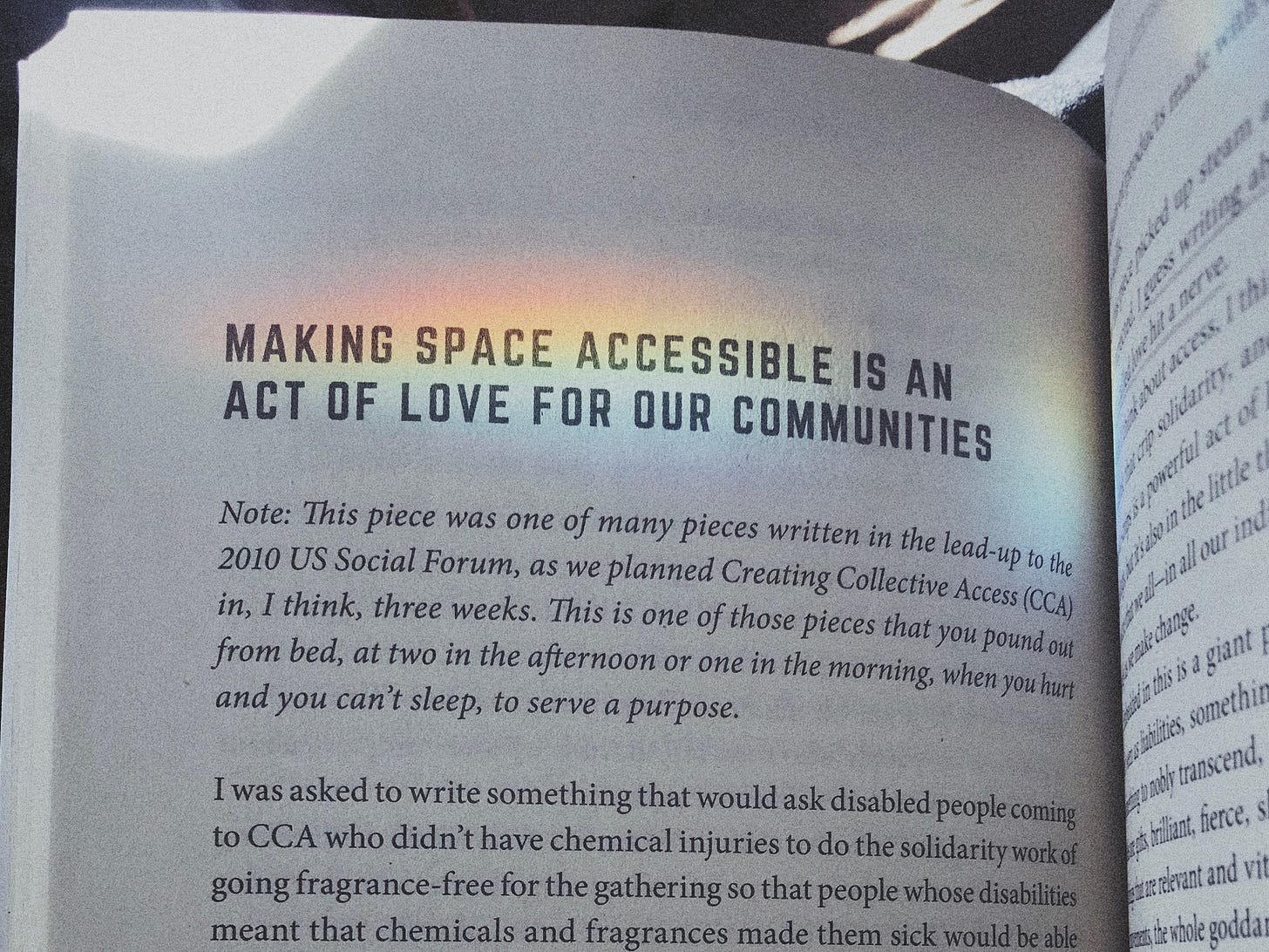 the book is open to a title page of a chapter that reads "Making Space Accessible Is an Act of Love For Our Communities." There is a strip of rainbow-colored light across the text.