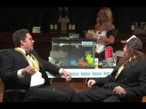 Two men sat on chairs in the foreground. Lady walks up behind them and throws a bunch of dollar bills in the air. Two men sat on chairs in the foreground. Lady walks up behind them and throws a bunch of dollar bills in the air.