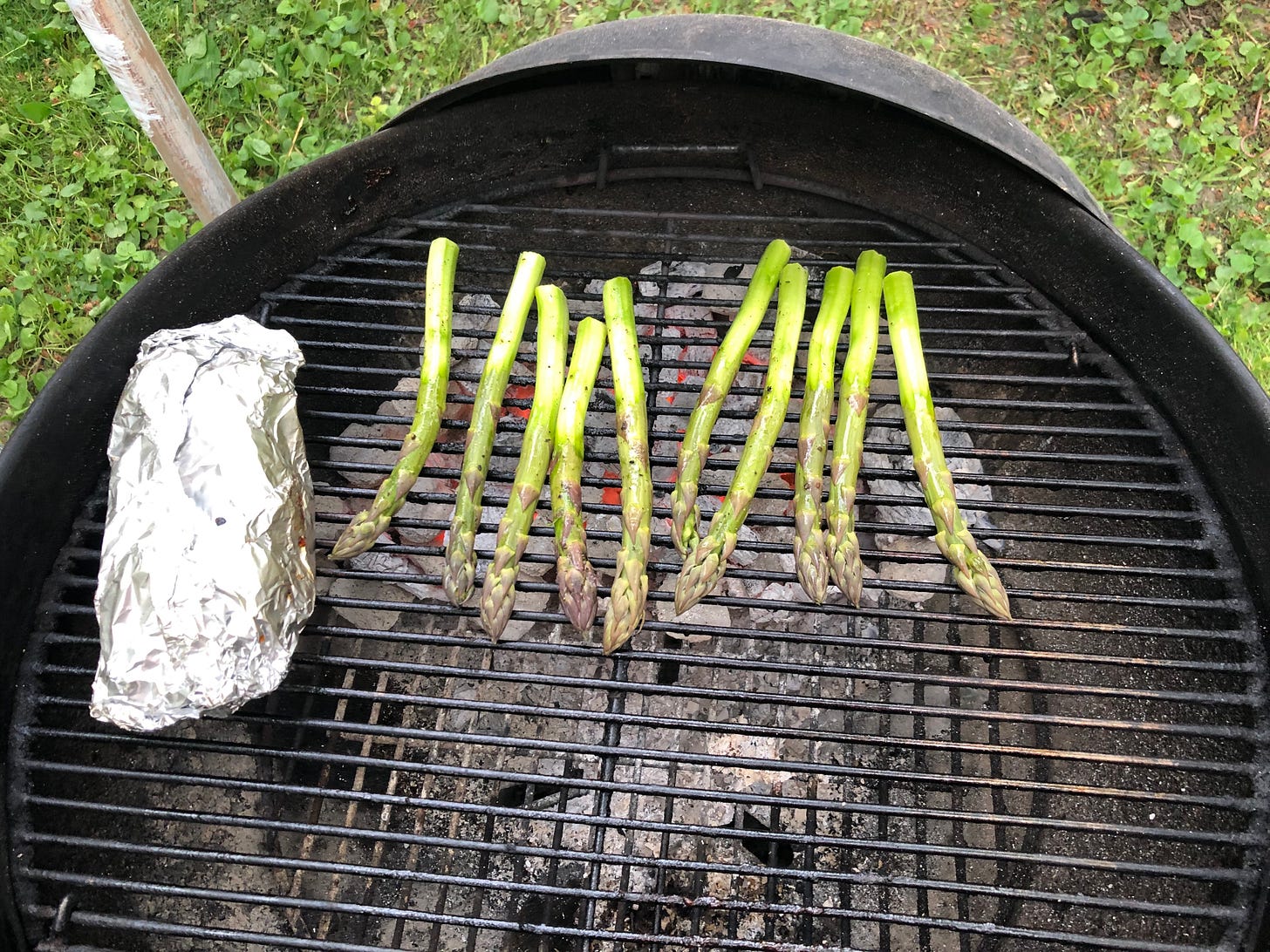 Asparagus grilling on a hot charcoal grill. Beside them on the grill is a foil packet. Asparagus grilling on a hot charcoal grill. Beside them on the grill is a foil packet.
