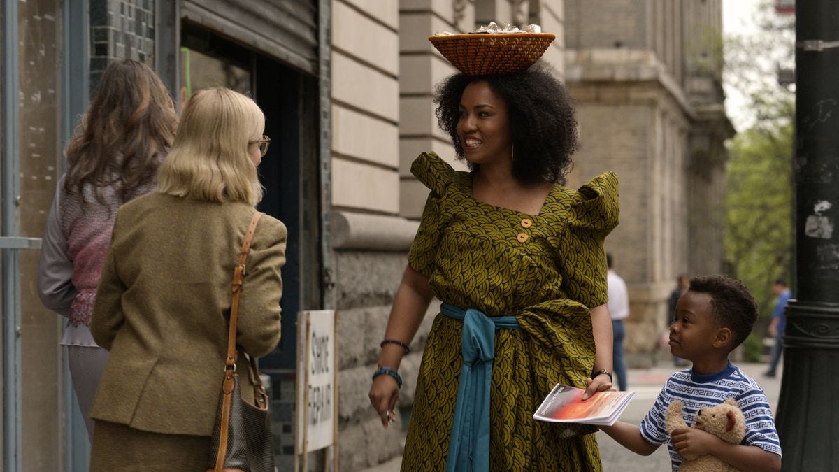A woman carrying a basket on her head leads her son, who holds a stuffed bear, in Little America