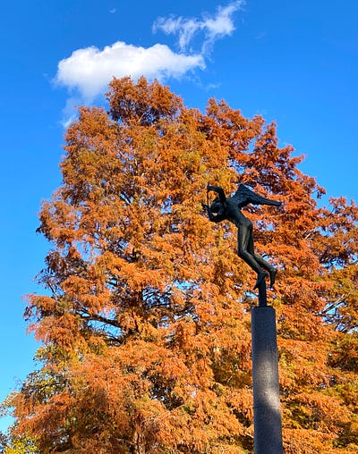 Angel musician statue silhouette in front of tree with orange leaves